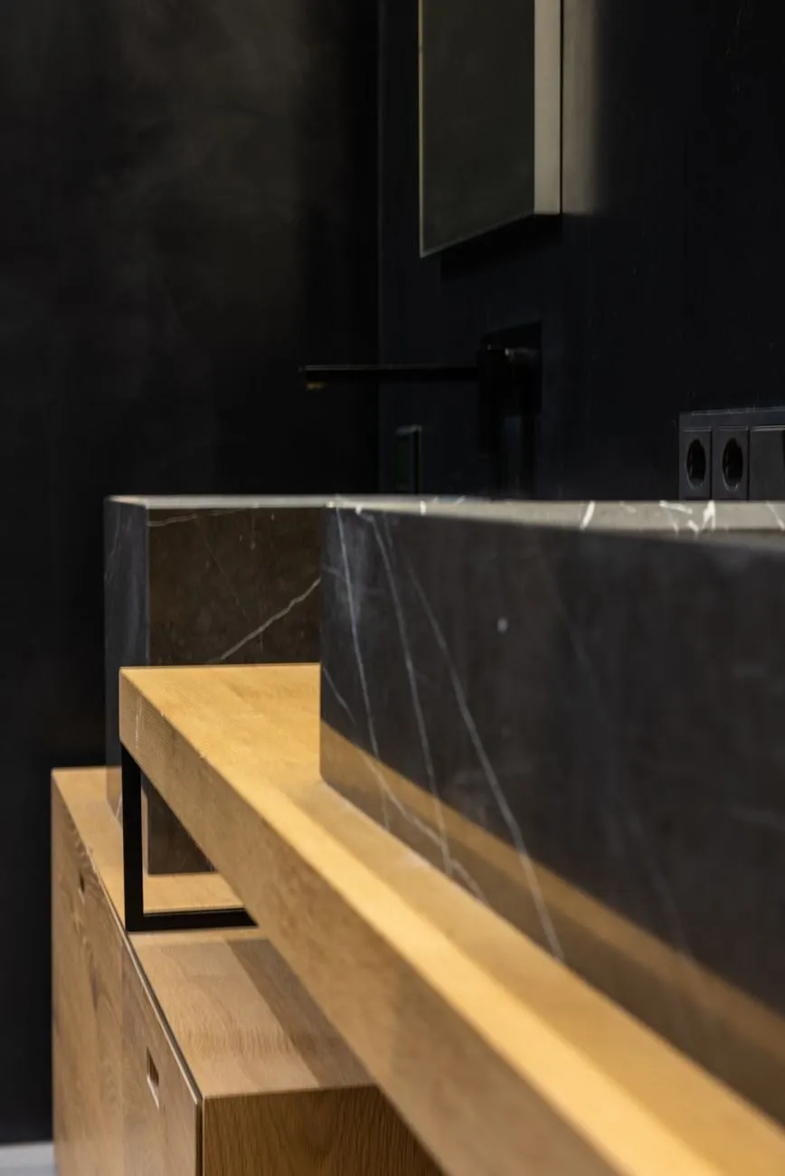 Close-up of a black marble basin with a matt black wall tap resting on a light oak vanity