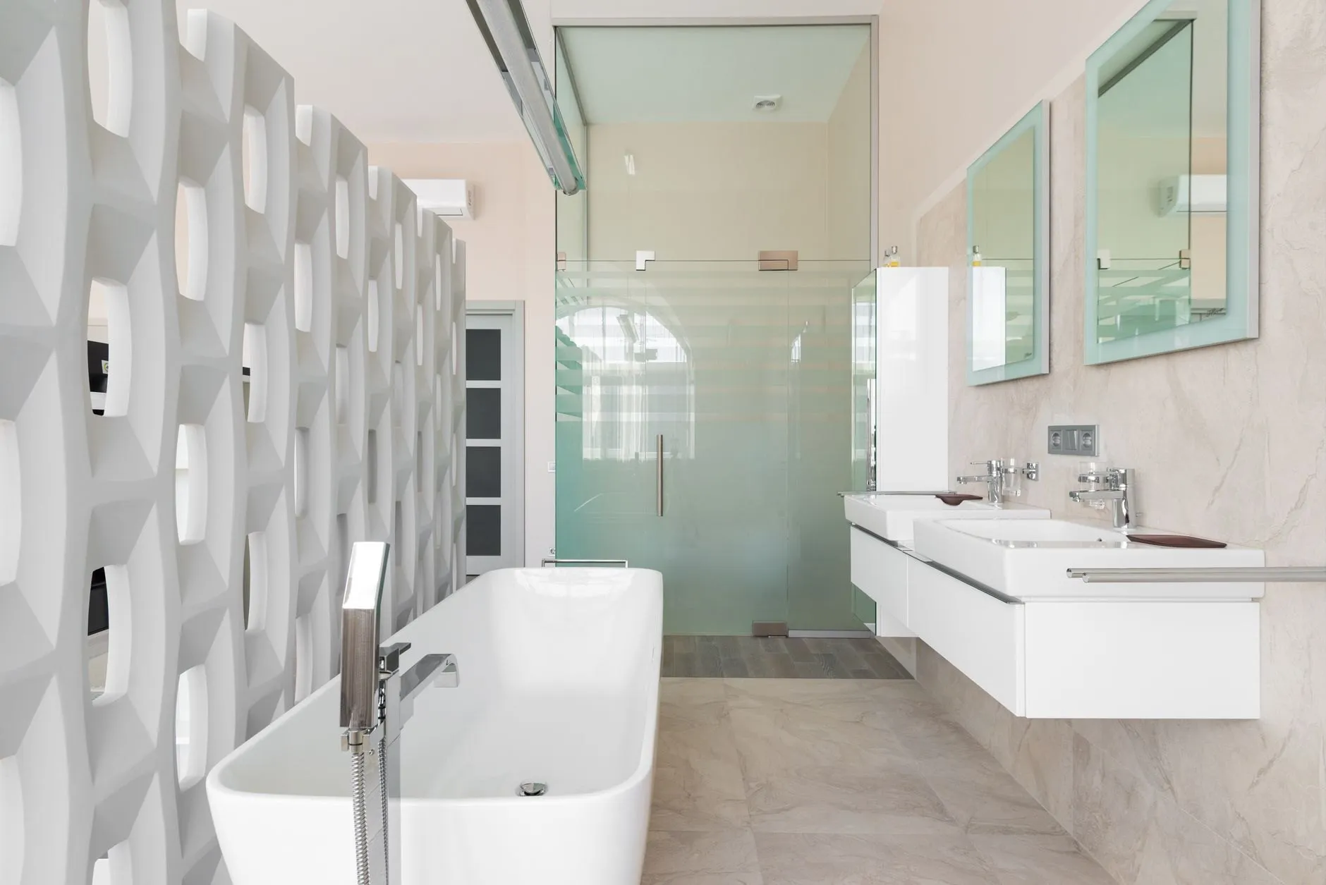 A bright bathroom with twin wall-hung basins, green-tinted mirrors, a glass shower enclosure and a bath behind a sculpted screen