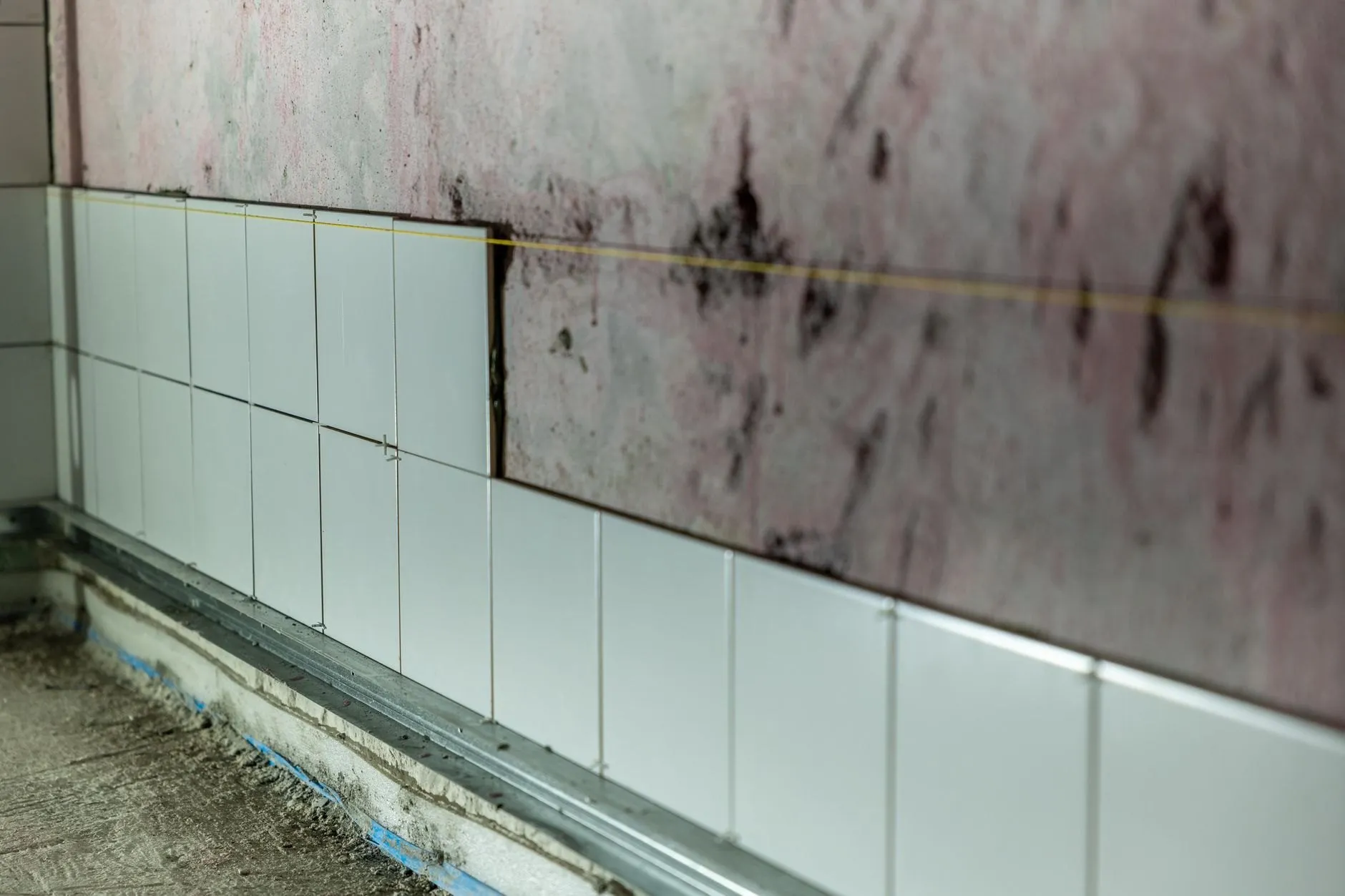 The same bathroom mid strip-out, the old white tiles half removed to bare, stained plaster above a lead-lined floor