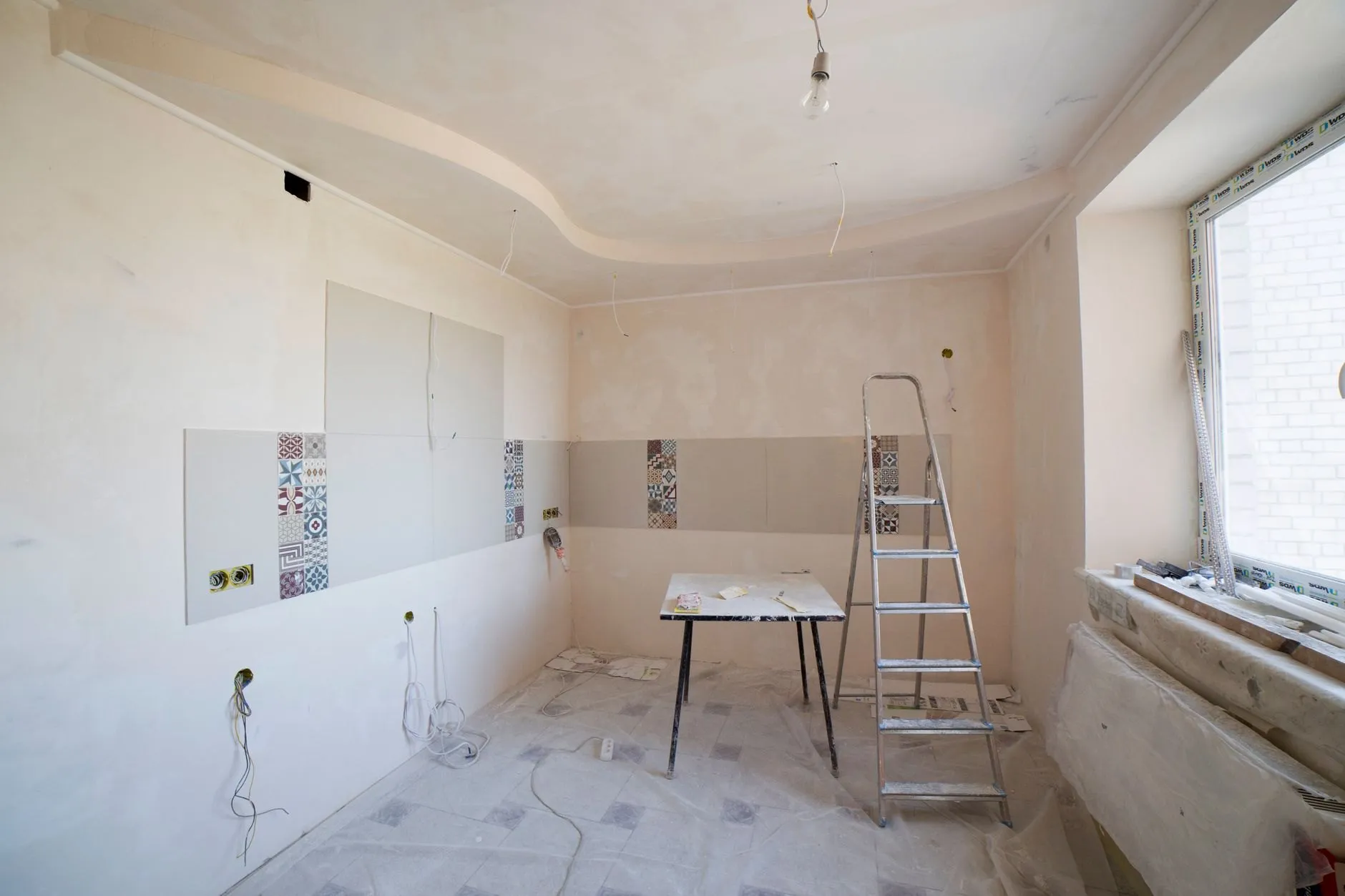 The same room stripped to plaster, with a stepladder, a paste table and a strip of test tiles on the bare wall