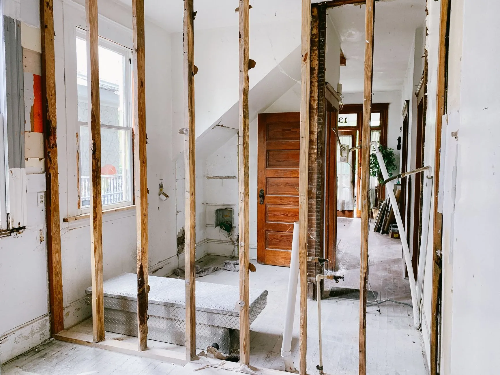 A partition wall stripped to its timber studs mid knock-through, with a hallway visible beyond