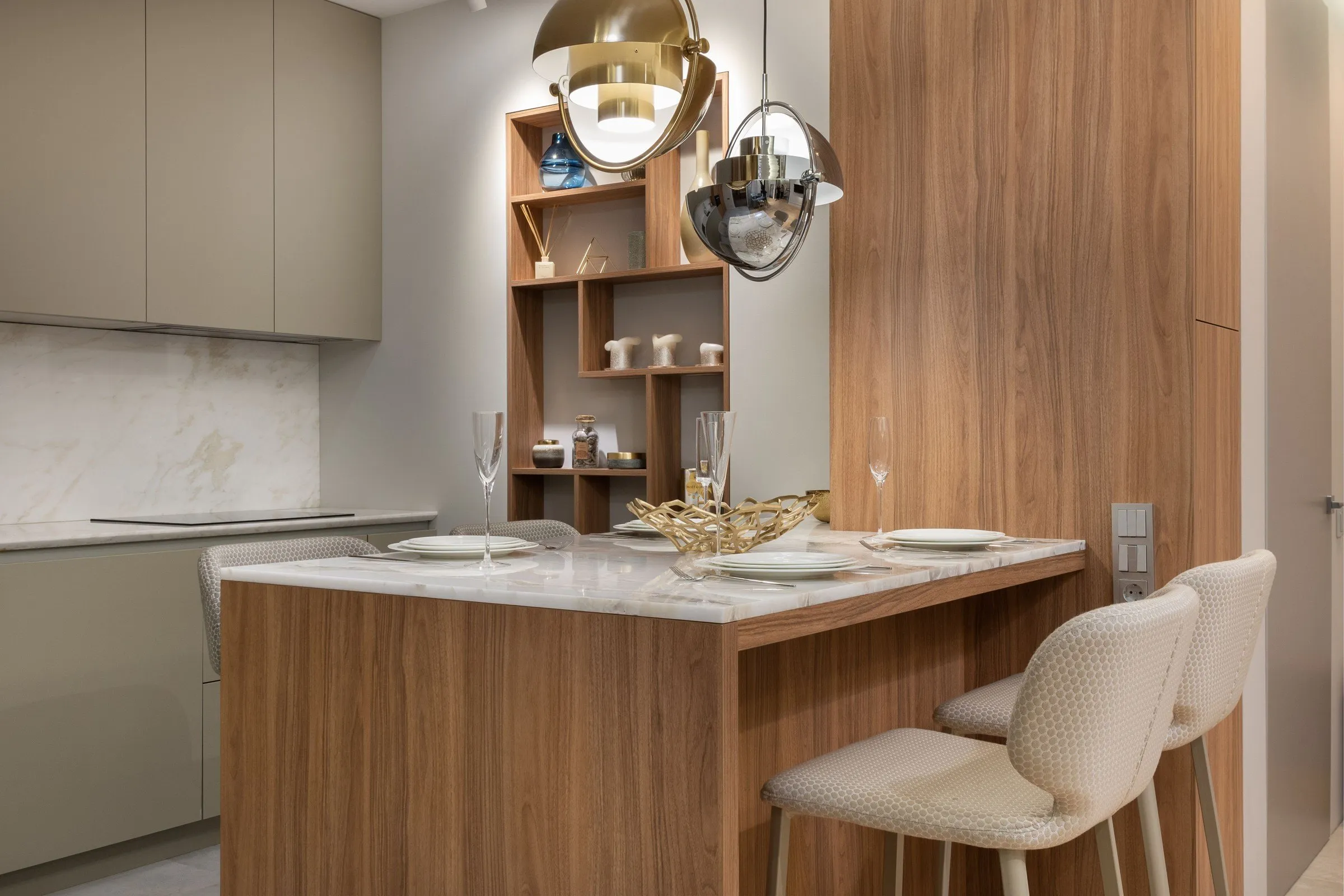 A finished kitchen with sage handleless units, a marble splashback, a walnut breakfast bar with a marble top set for dinner, and brass and chrome pendant lights