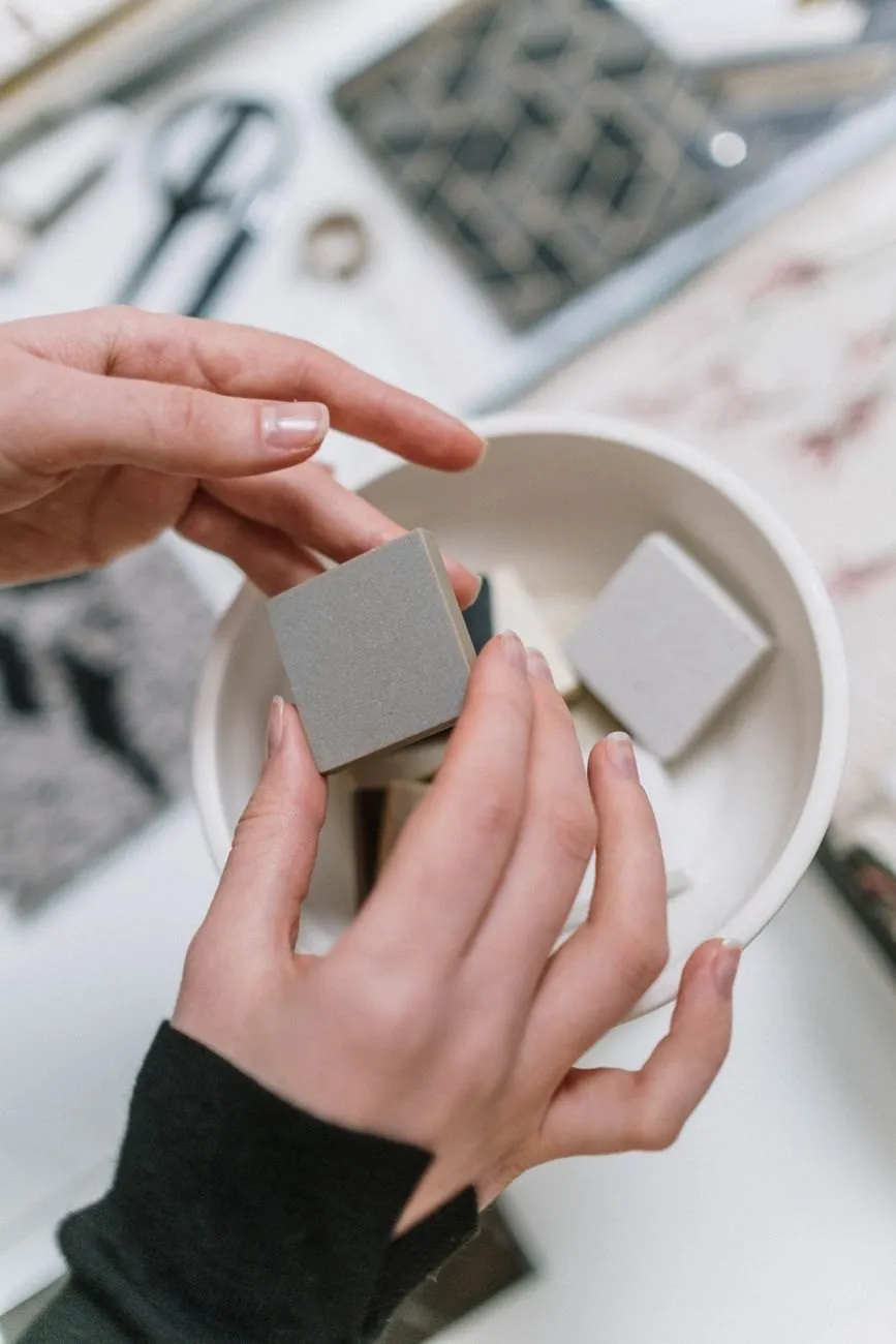 Hands holding small grey and white ceramic tile samples over a bowl