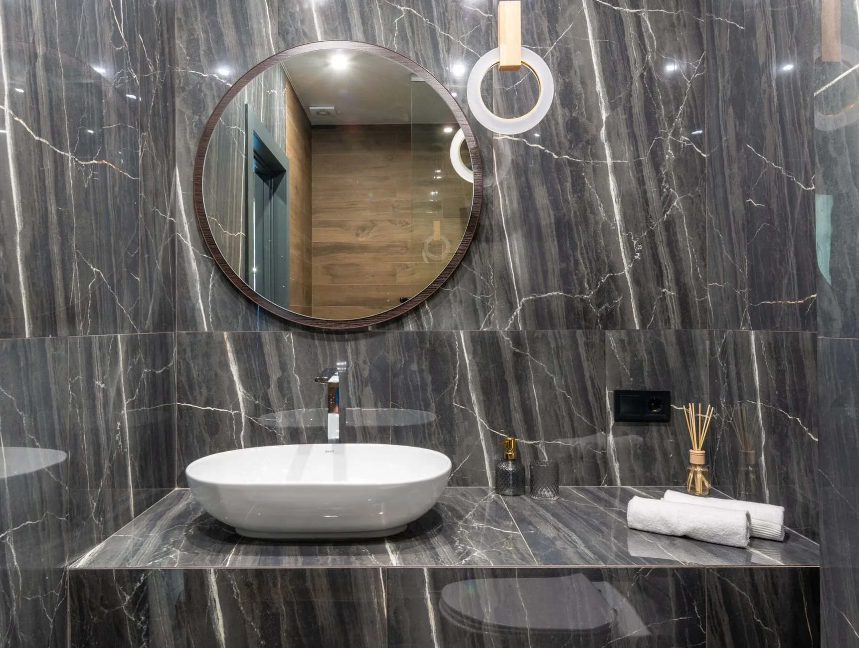 A white vessel basin on a dark veined marble vanity under a round wood-framed mirror