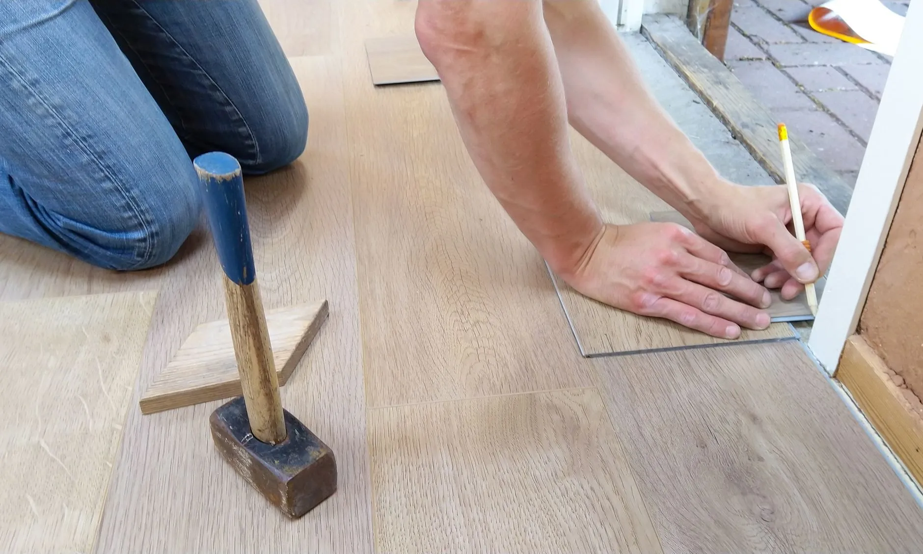 A fitter kneeling on a new floor, marking a plank with a pencil and square