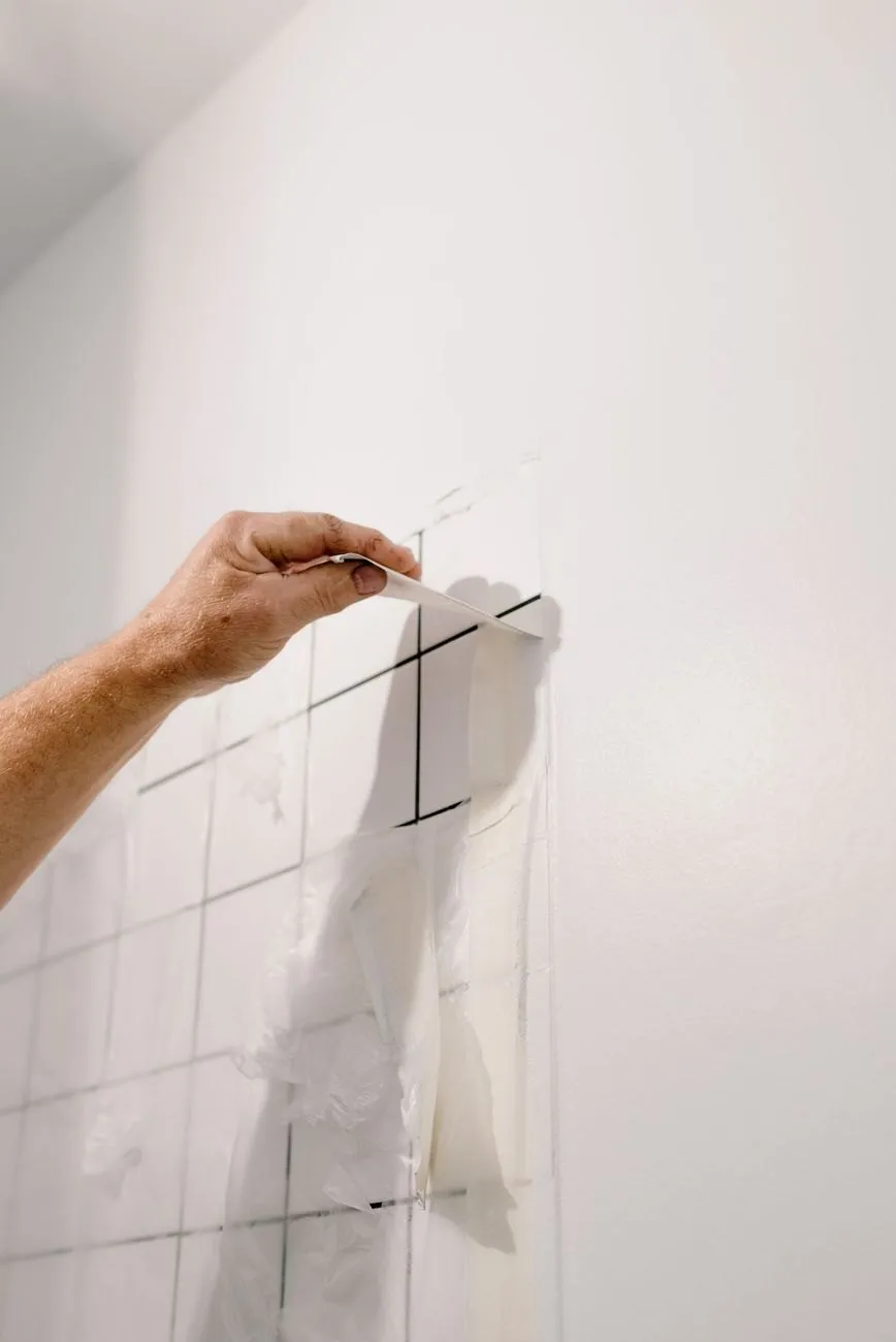 A hand marking tile positions in pencil on a freshly plastered wall